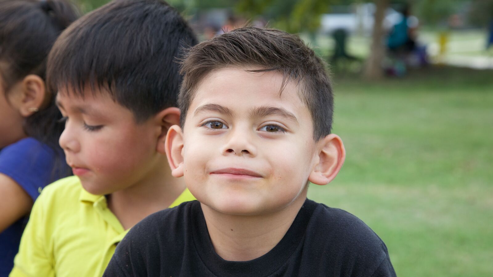 A young boy sitting on grass and smiling