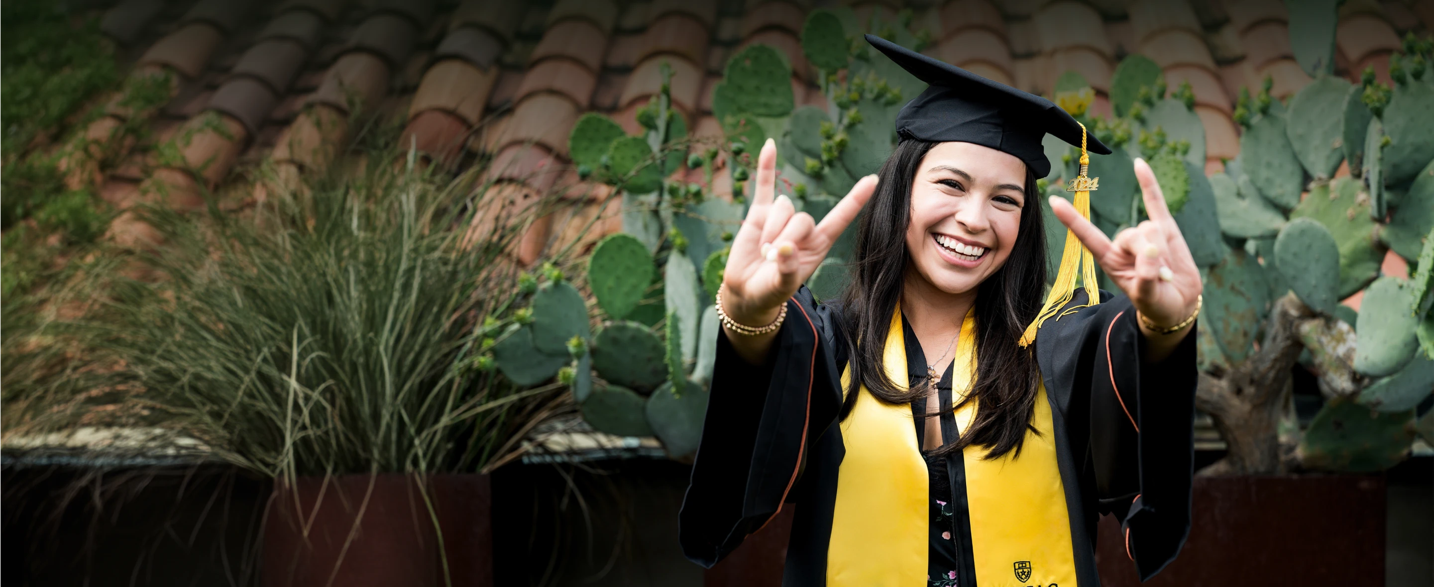 Woman in graduation gown smiling and making hook 'em horns sign.