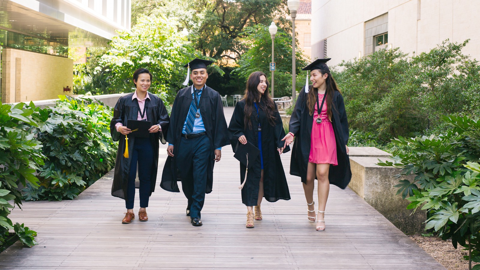 Four graduates walk down a pathway together.