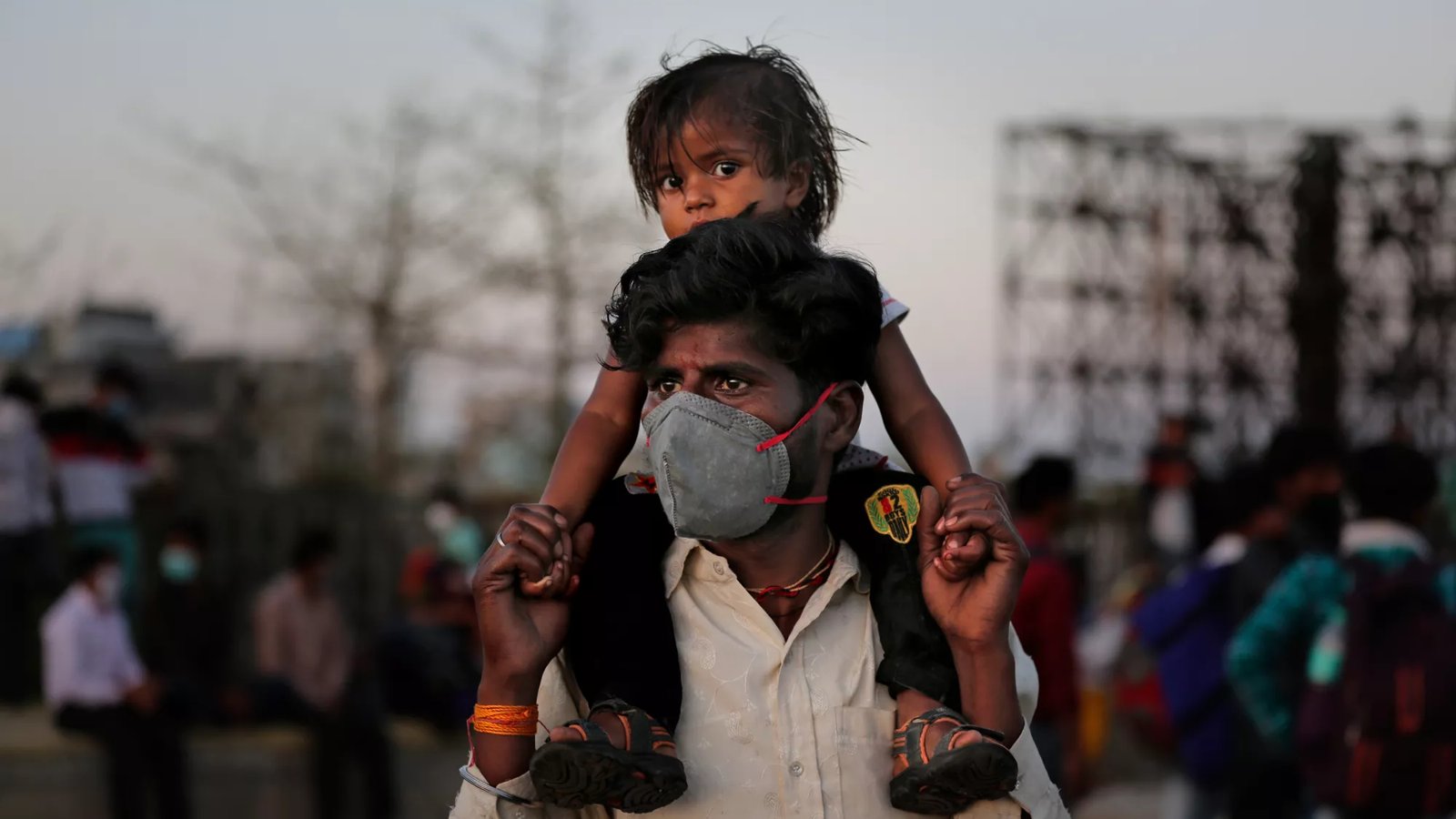 An Indian father in a mask carries his child on his shoulders.