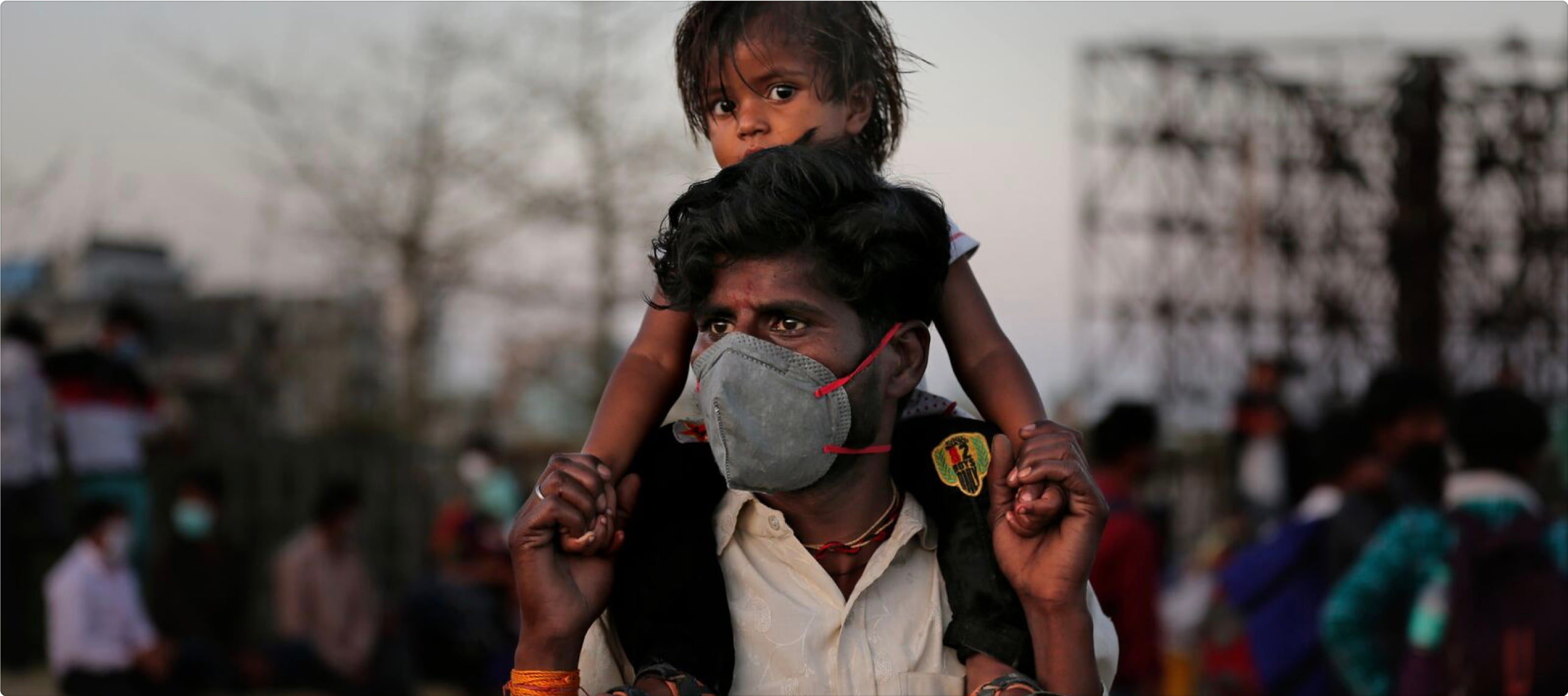 An Indian father in a mask carries his child on his shoulders.