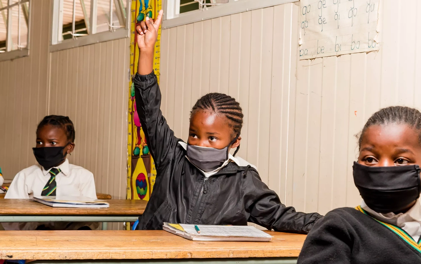 A South African student in a mask raises his hand in class.