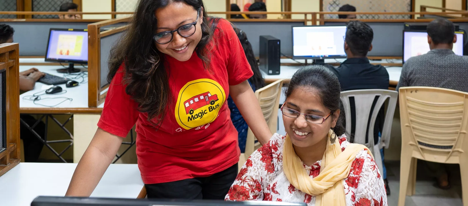 Two young Indian women look at a computer screen.