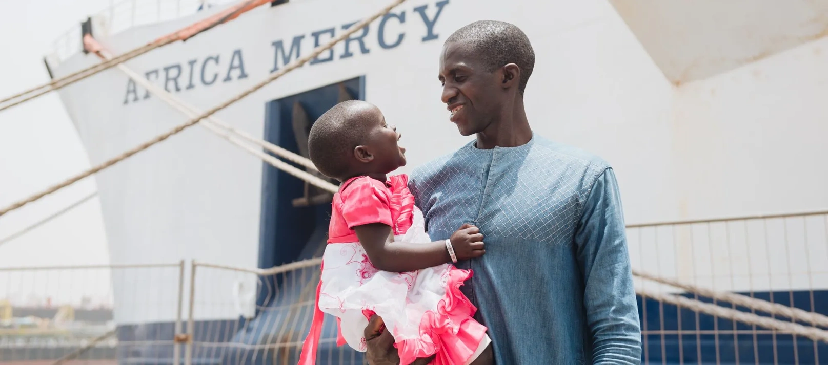 A father holds his child in front of a hospital ship.