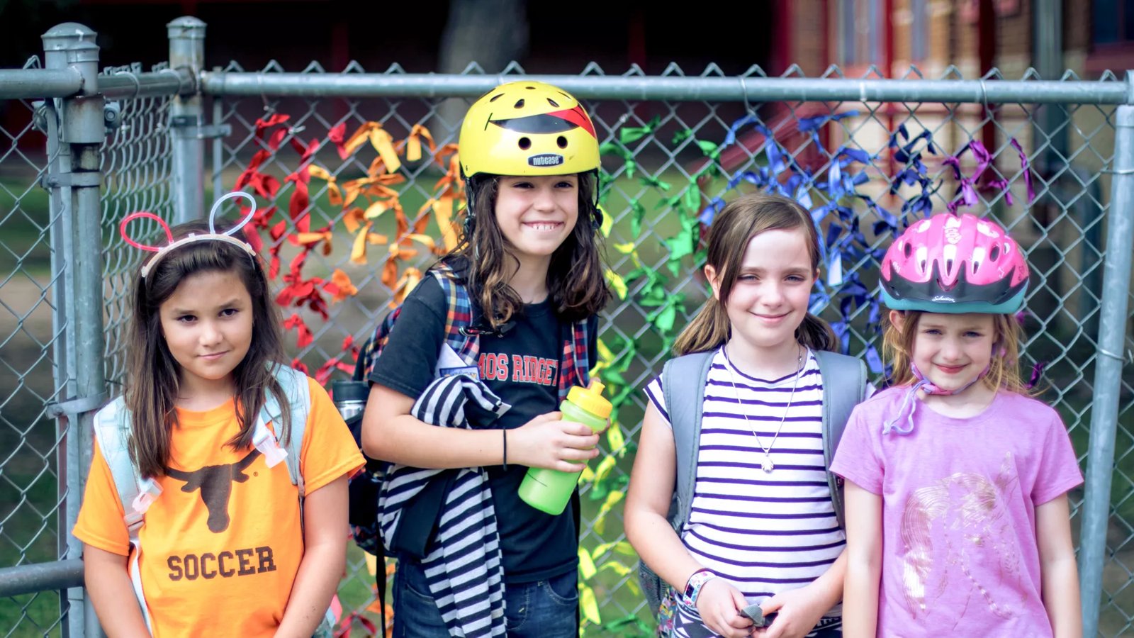 Four girls stand outside in front of a park fence.