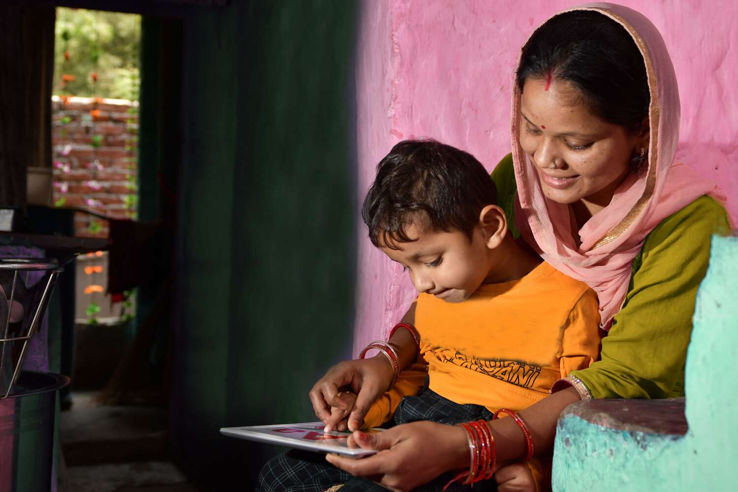 A mother sits with her child as he learns on an iPad.