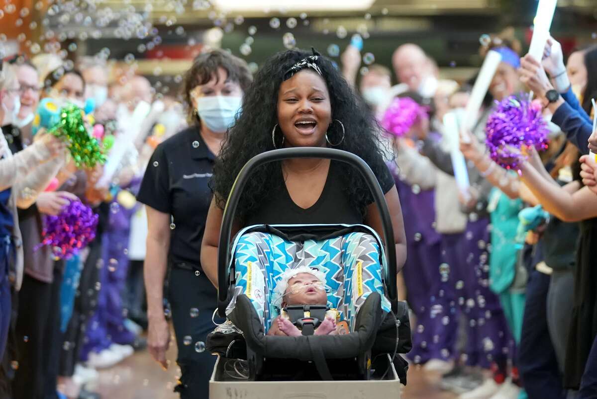 A mother and her baby in a stroller surrounded by celebrating medical professionals.