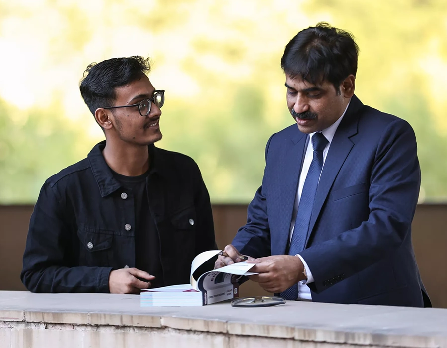 A student and a professor look at a book together on campus.