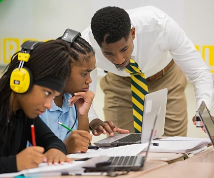 A teacher assists two students in a classroom.