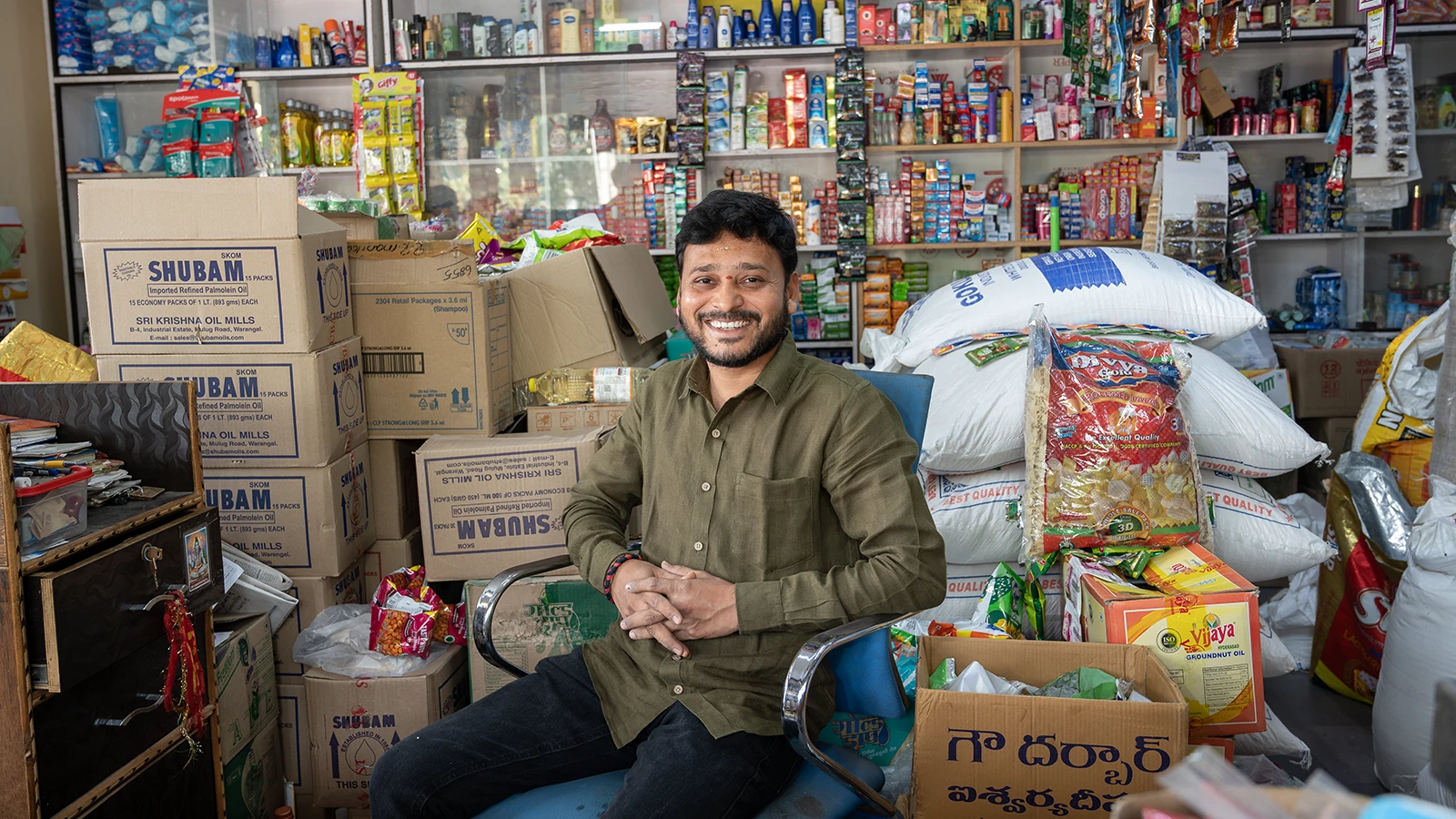 A man sits in a shop, surrounded by inventory.