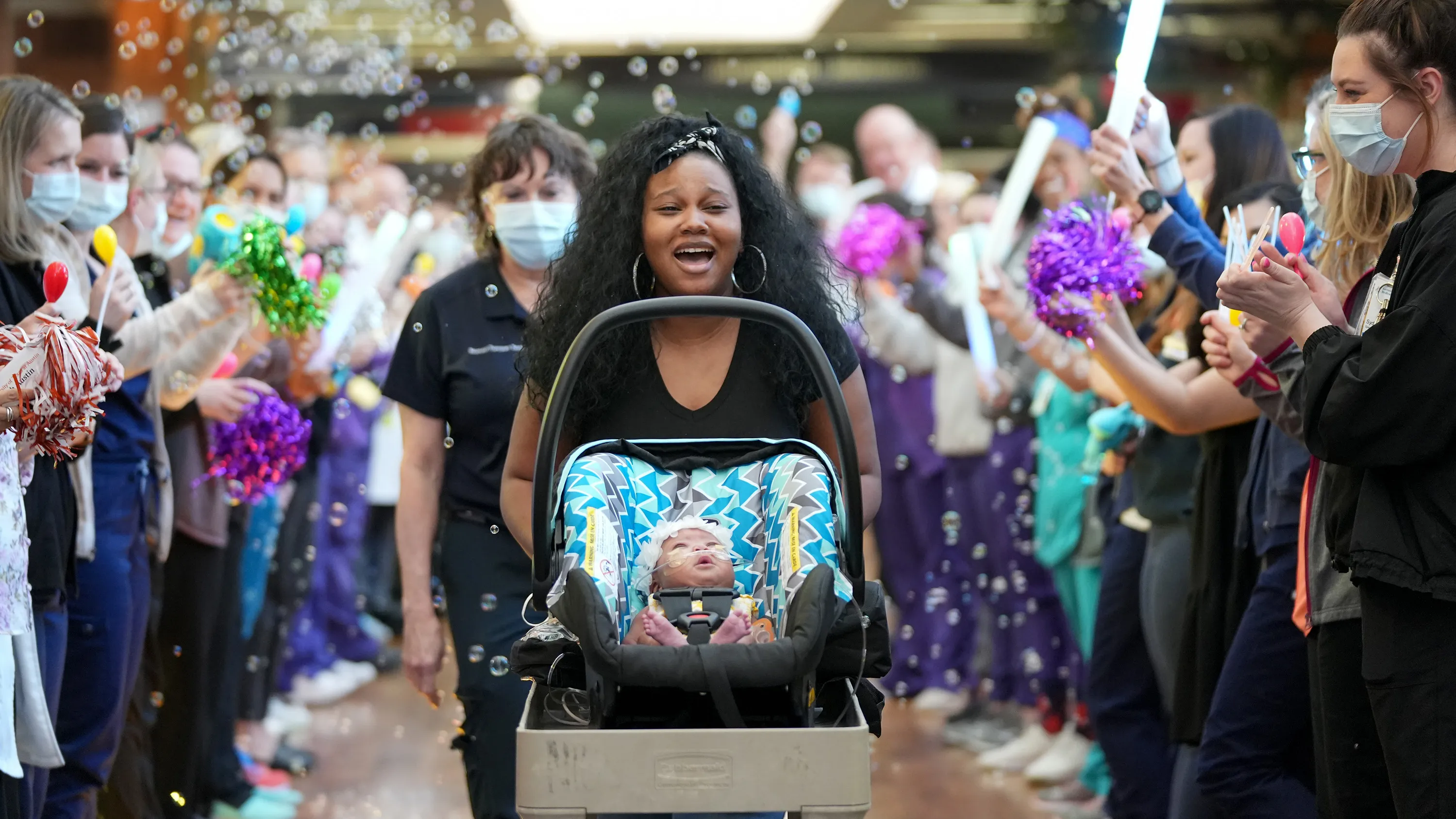 Woman pushing newborn surrounded by celebratory crowd.