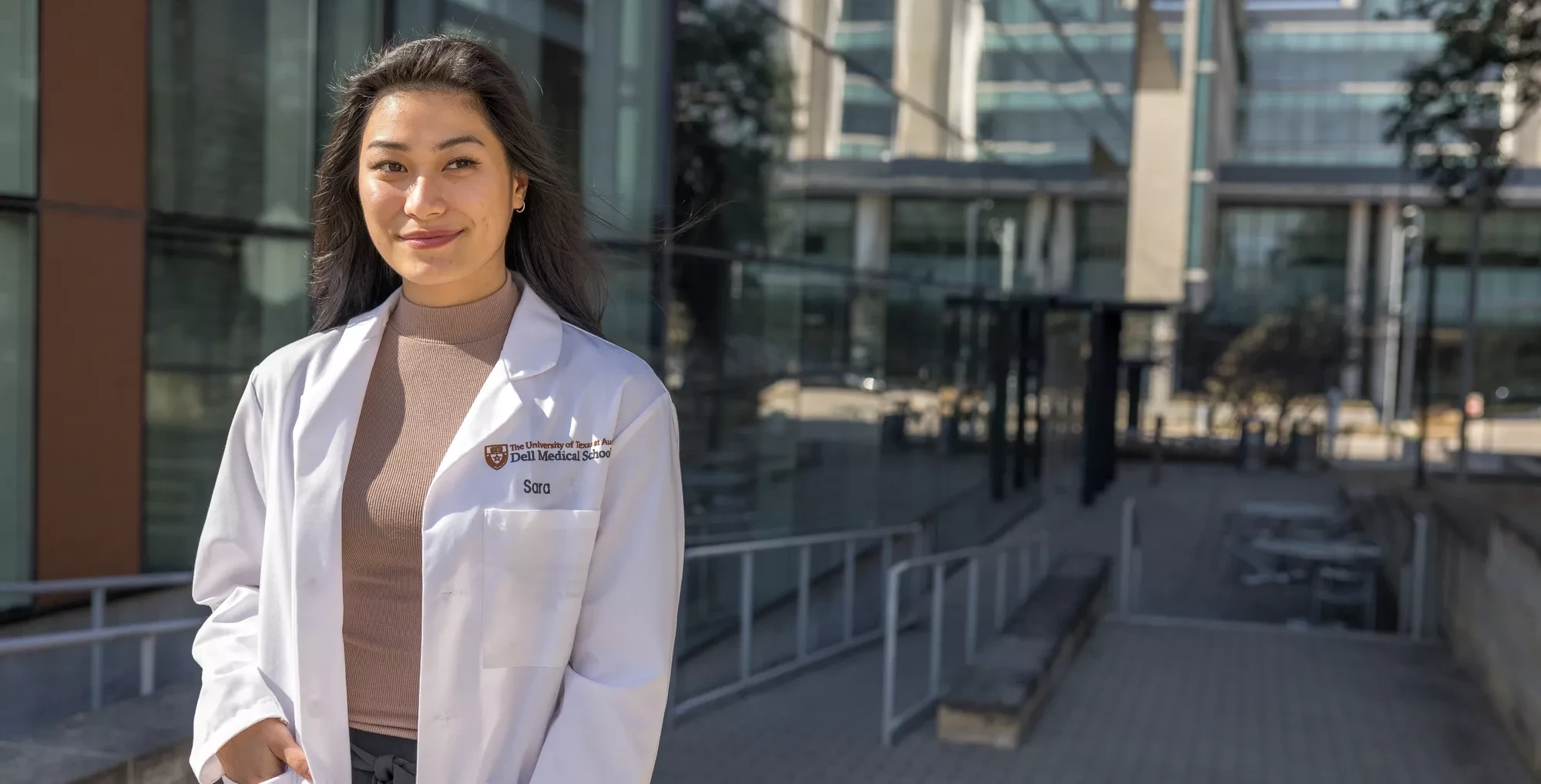 A smiling Dell Medical School student stands in front of a glass building.