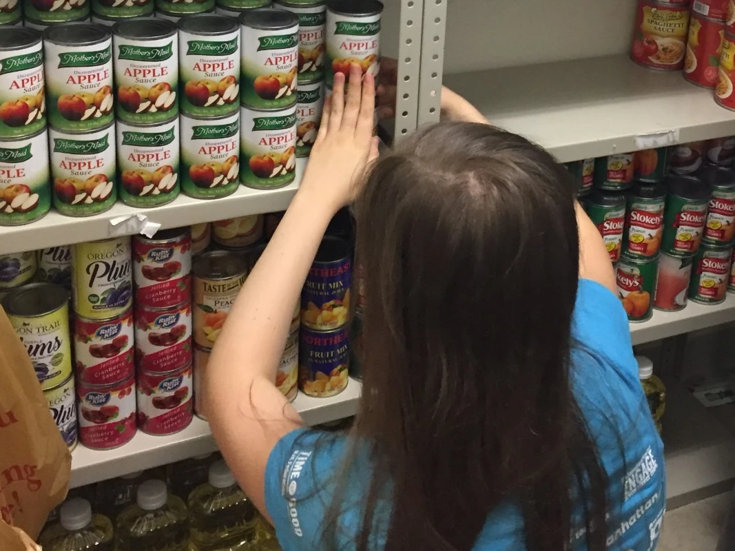 A woman stocks cans of food on a pantry shelf.