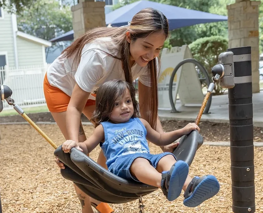 A woman pushes a young child on a swing at the playground.