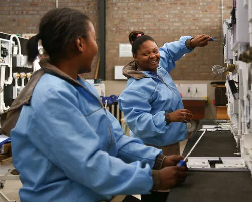 Two women in blue jackets operating a machine in a professional setting.