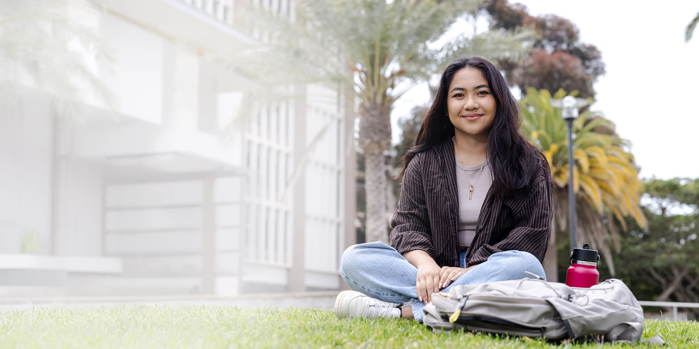 A woman sits on the grass on a college campus.