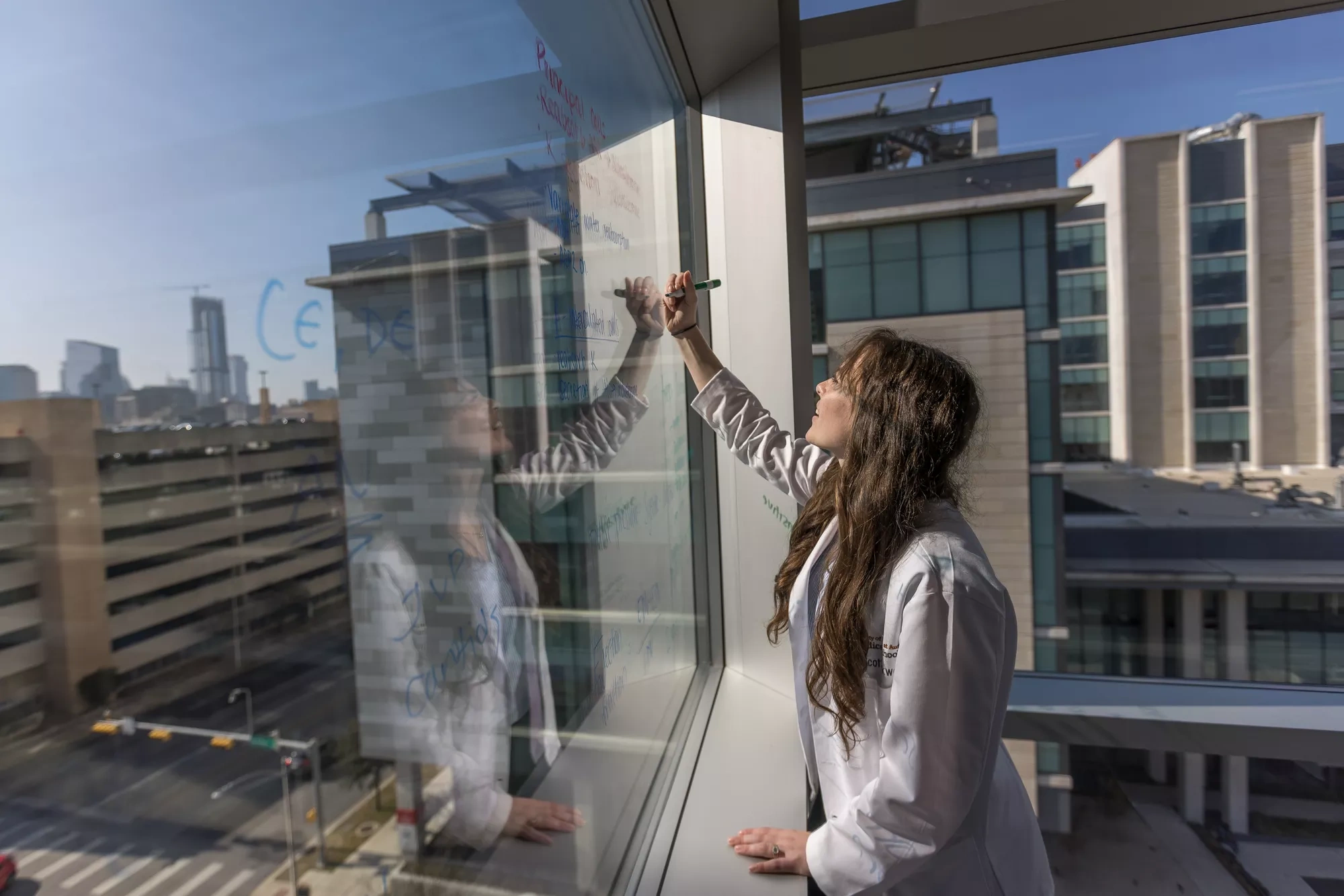 A medical student writes on a window board, surrounded by buildings.