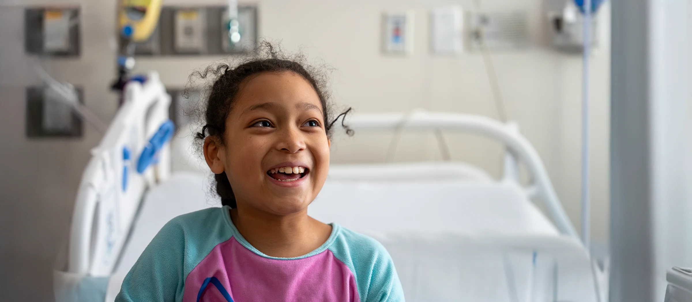 A young girl smiles while sitting on a hospital bed.