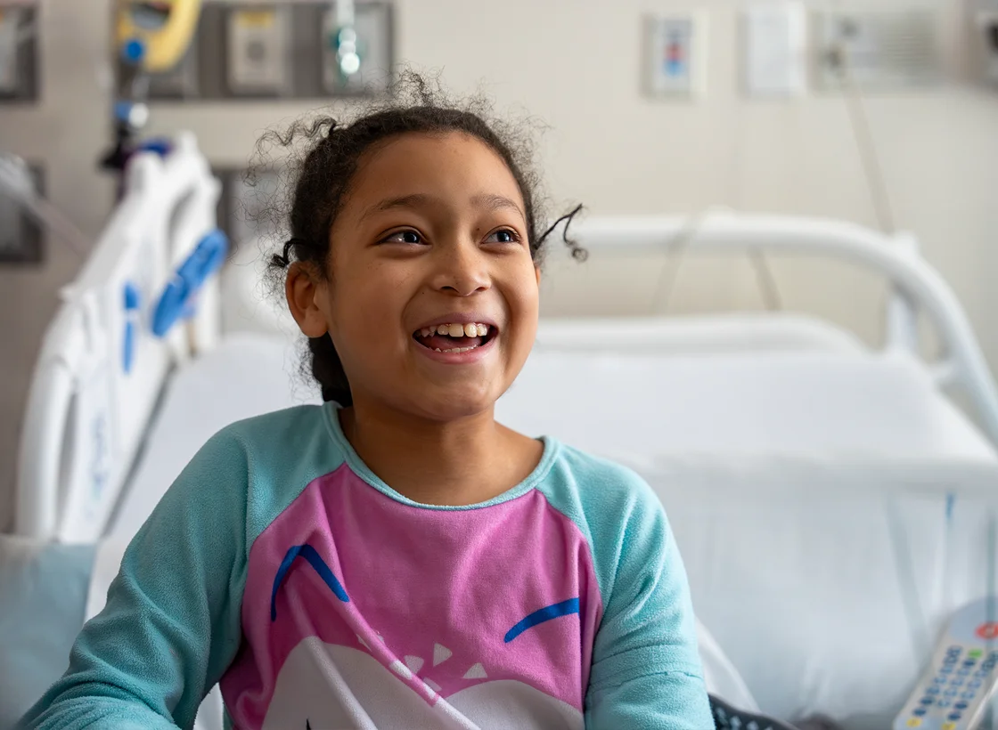 A young girl smiles while sitting on a hospital bed.