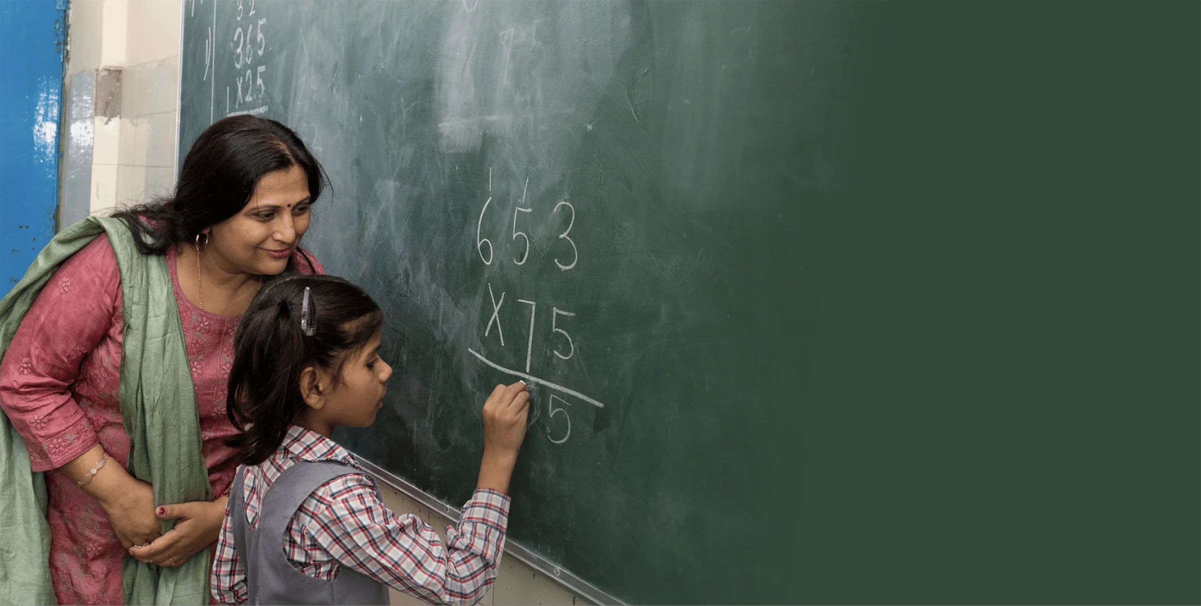 A woman and a girl writing on a blackboard in a classroom.