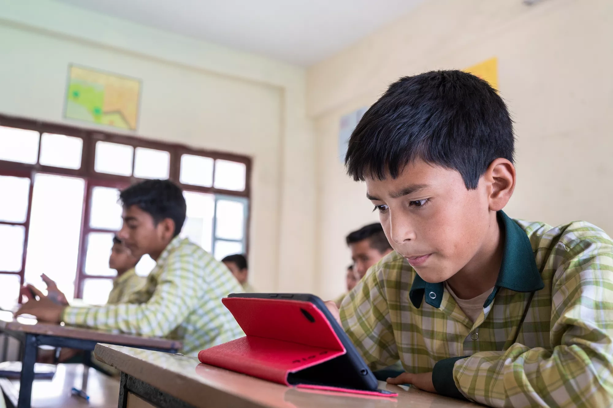 A boy looks at a tablet in a classroom.