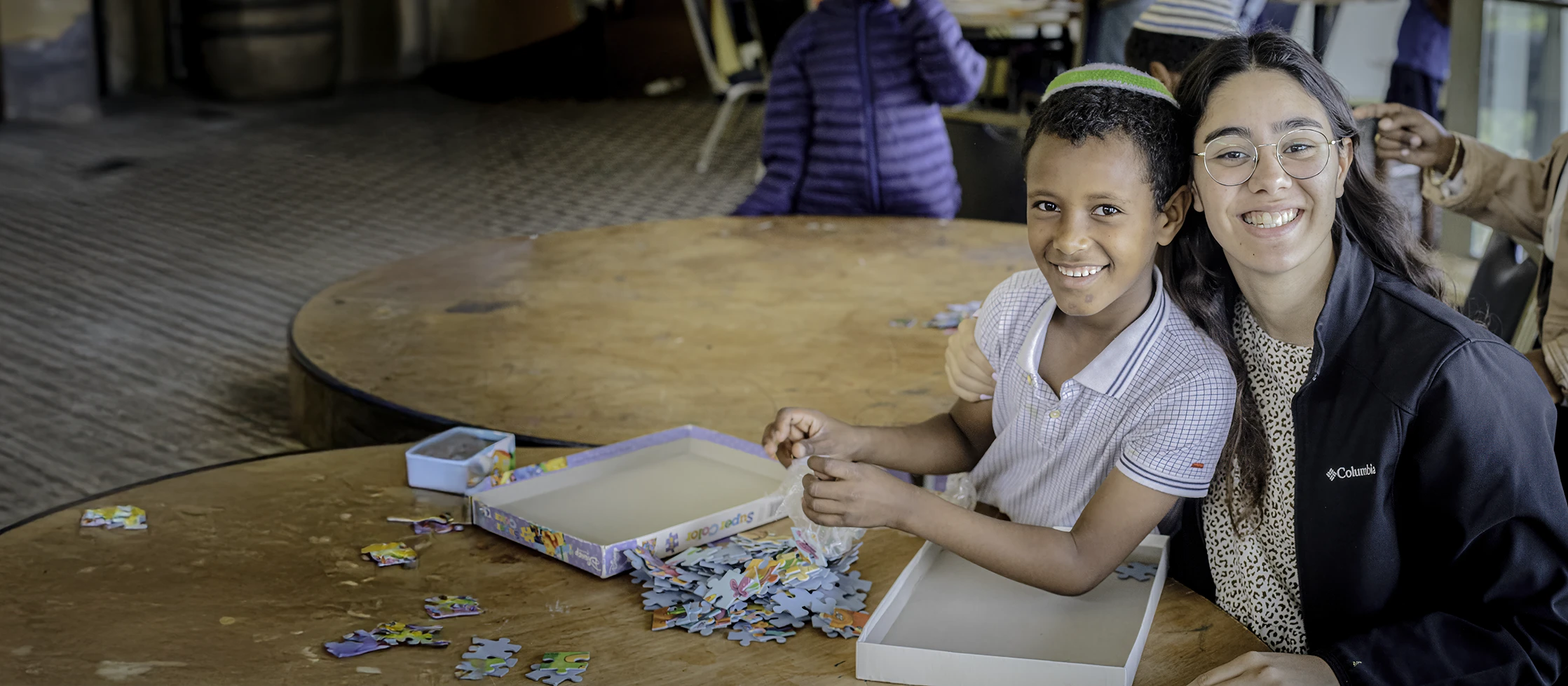 A woman and a child smiling while doing a puzzle.