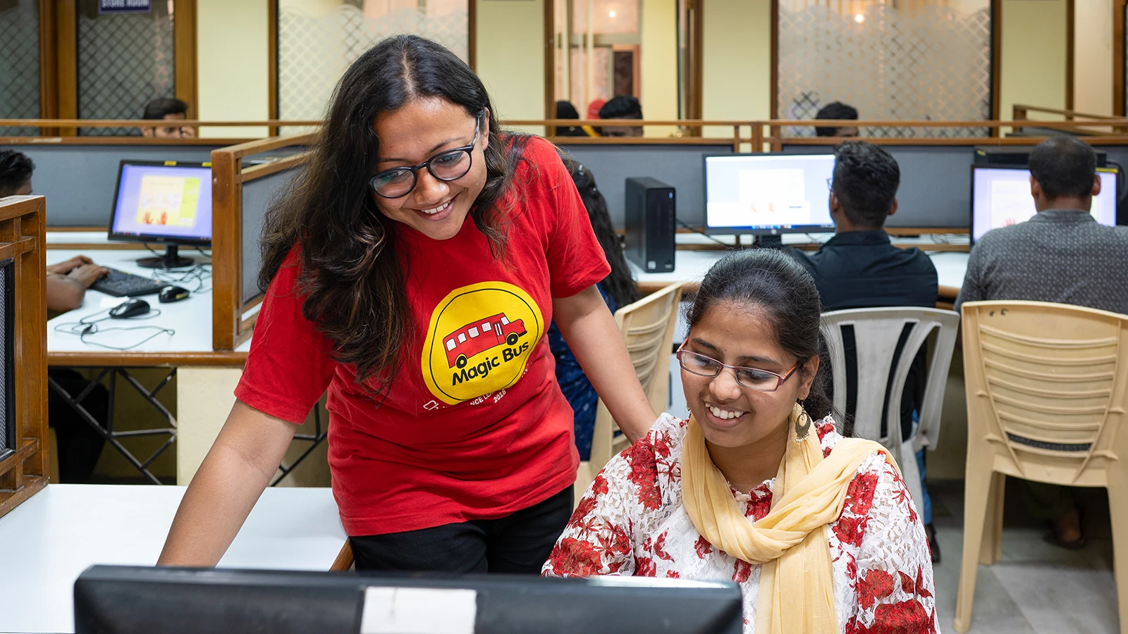 Two women look at a computer screen in an office setting.