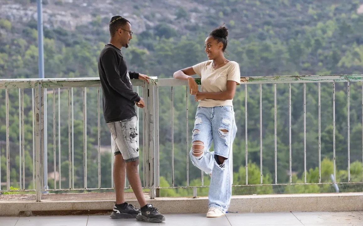 Two people stand on a balcony, chatting.