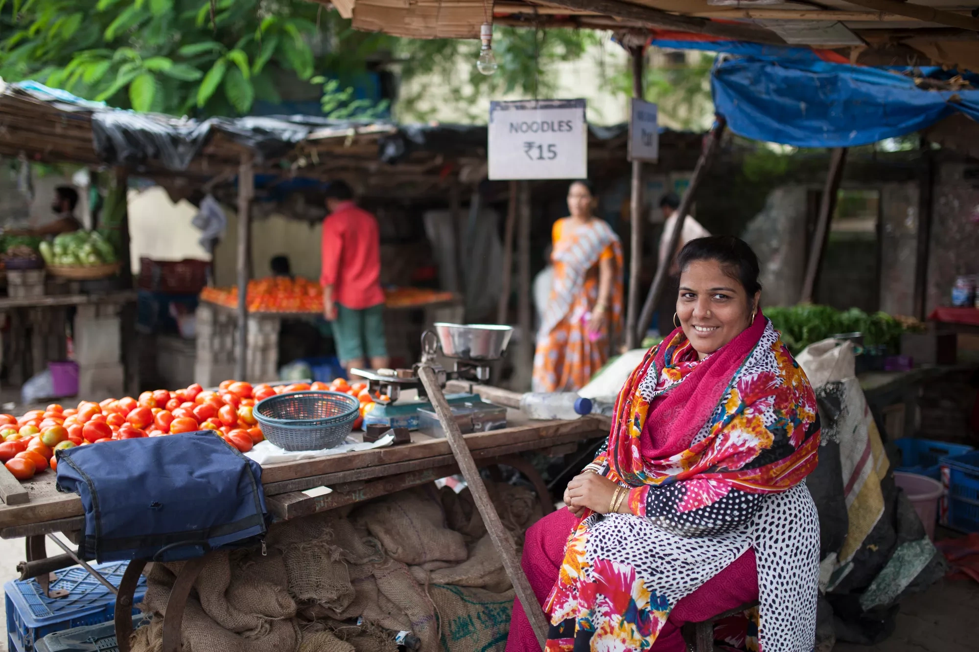 Woman sitting near her food stall, looking into the camera and smiling.