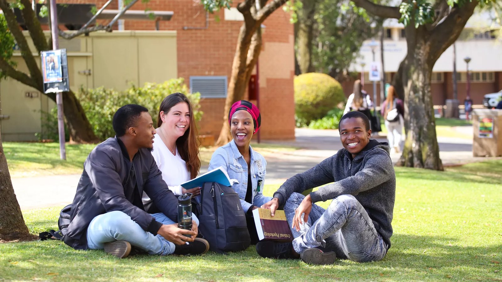 A group of South African university students sit on the grass on campus.