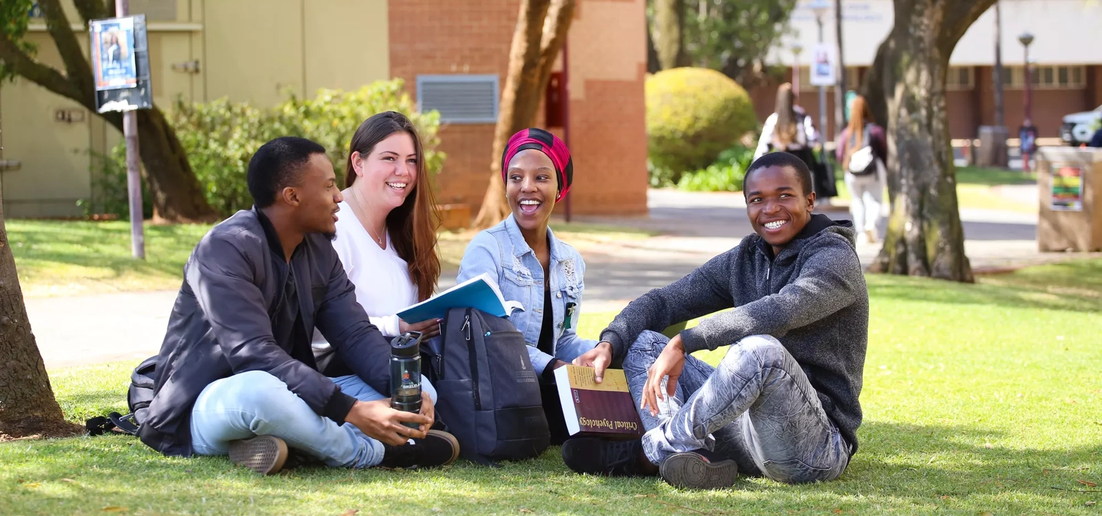 A group of South African university students sit on the grass on campus.