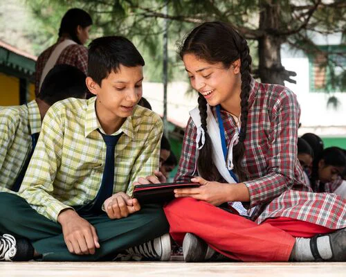 Two young individuals seated on the ground, sharing a tablet device.