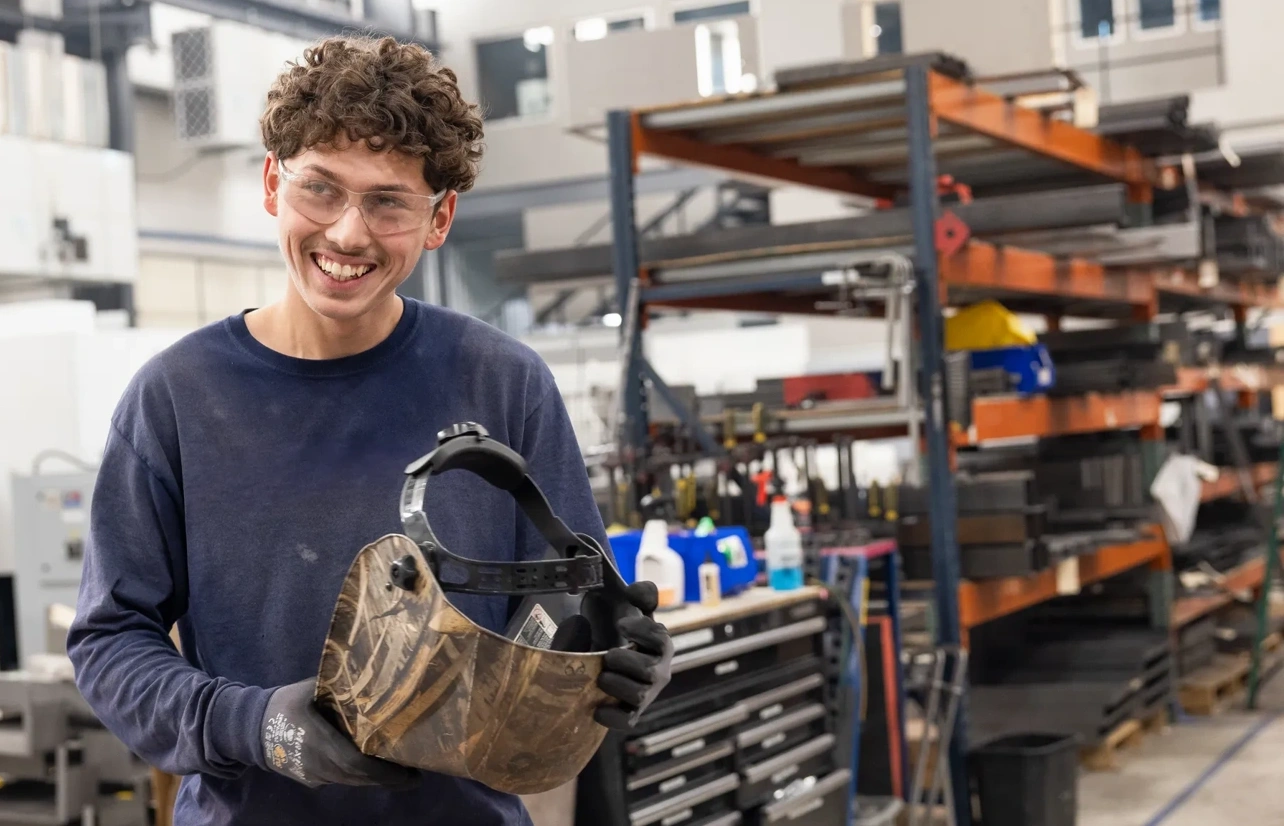 Kristian Charles smiles while holding a welding helmet at Athena Manufacturing in Round Rock, Texas.