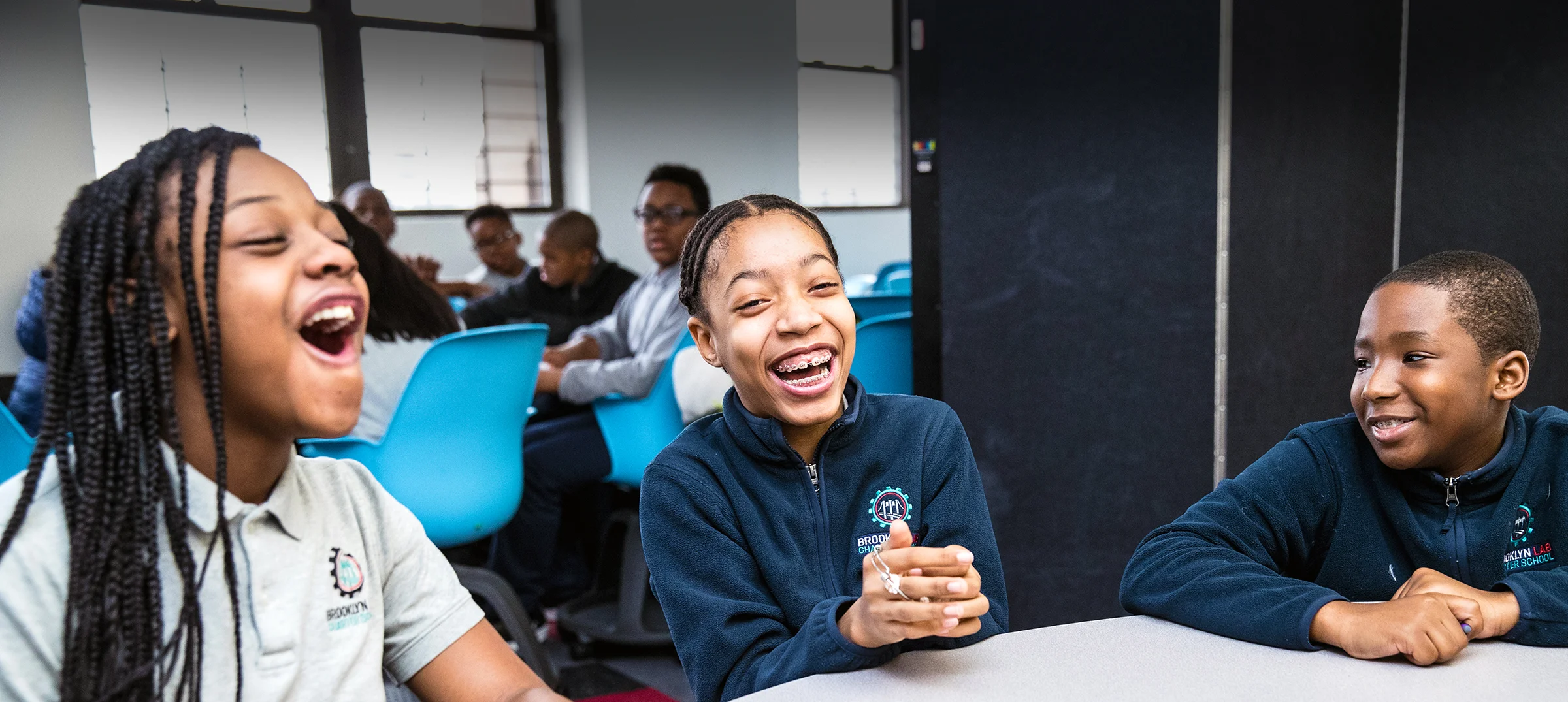 Three students laugh at a lunch table.