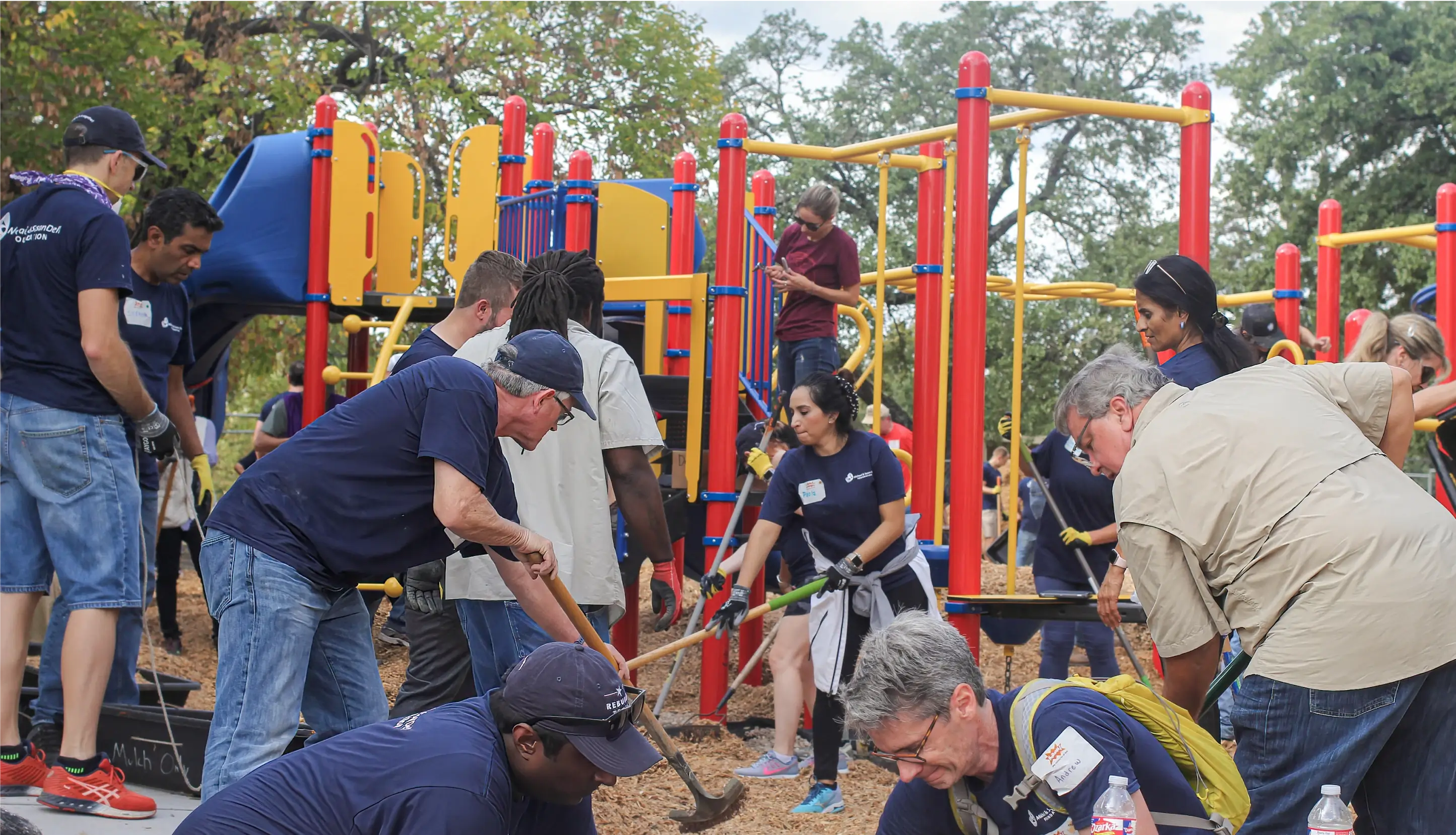 A large group of people shoveling mulch into a playground.