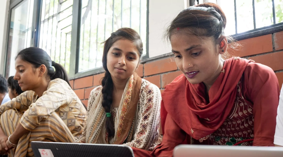 Two women look at their laptops together.