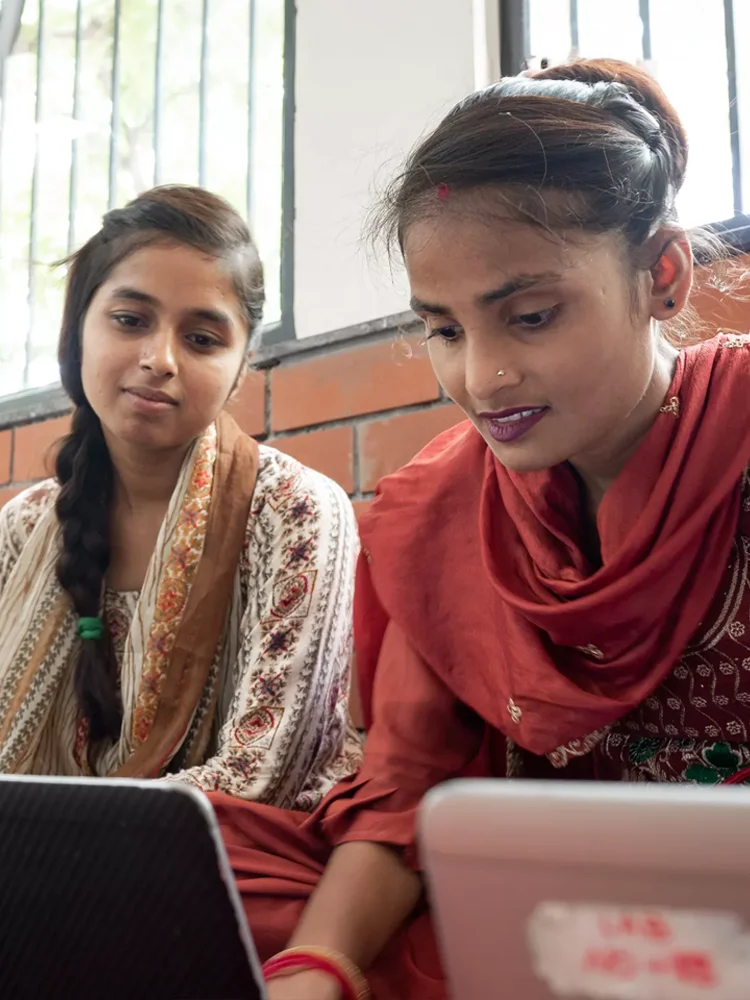 Two women look at their laptops together.